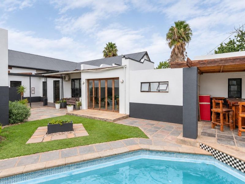 A well-maintained rear exterior featuring a swimming pool, stone-paved patio area with a timber pergola, and direct access to the home via bi-fold doors.