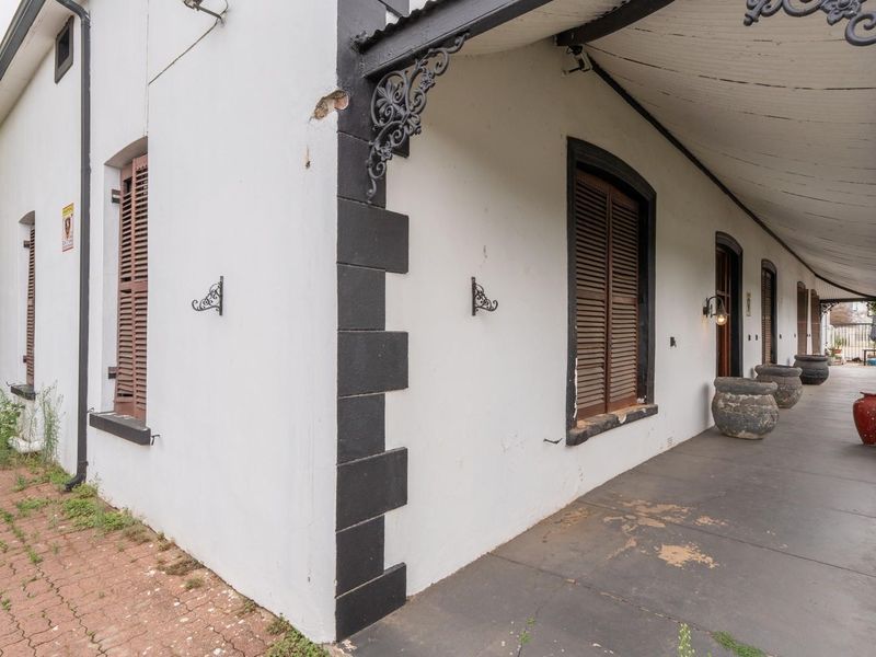 A covered veranda featuring classic wrought iron detailing, timber shutters, and paved flooring, offering a charming outdoor space with potential for cosmetic updates.