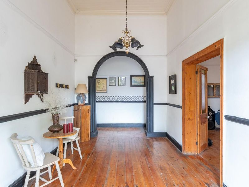 A spacious hallway featuring original hardwood flooring, a decorative archway, and classic architectural details including crown molding and chair rail trim.