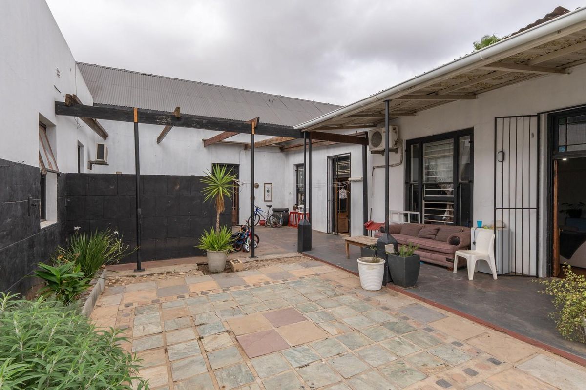 A rear courtyard featuring a paved patio area, a covered veranda, and a pergola structure, offering potential for outdoor living and entertainment space.