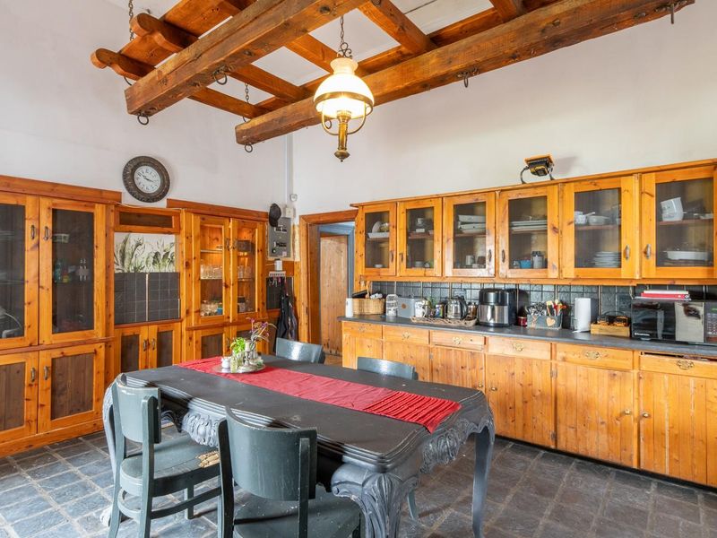 Spacious kitchen featuring rustic exposed timber beams, extensive built-in wooden cabinetry, and durable stone tile flooring, offering a traditional and functional cooking space.