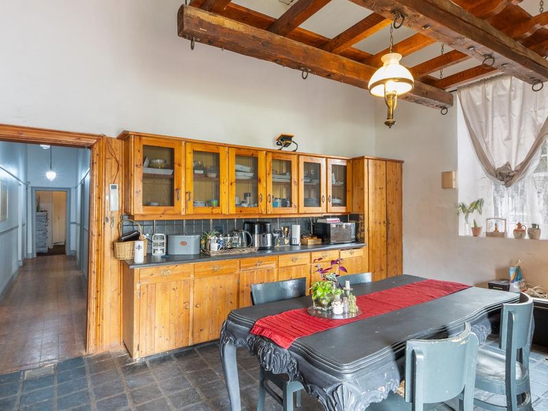 Open plan kitchen and dining area featuring rustic exposed timber ceiling beams, fitted wooden cabinetry, and durable slate tile flooring.