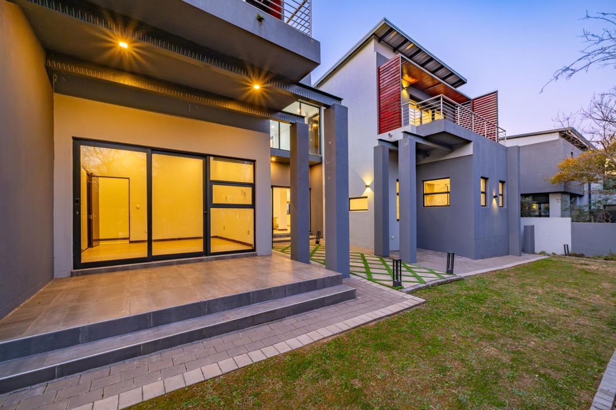 Modern rear exterior view featuring a spacious tiled patio, sliding glass doors, and a balcony with timber shutters, set against a well-maintained garden.