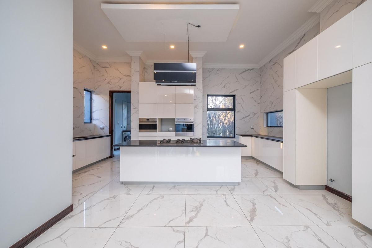 Modern, spacious kitchen featuring a central island, high-end built-in appliances, glossy cabinetry, and elegant marble-look wall and floor finishes.