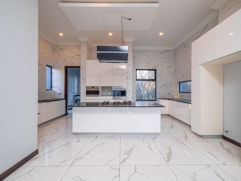Modern, spacious kitchen featuring a central island, high-end built-in appliances, glossy cabinetry, and elegant marble-look wall and floor finishes.
