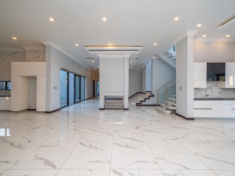 Spacious open-plan living area featuring high-end marble-look floor tiles, a central fireplace, modern staircase with glass balustrades, and a sleek contemporary kitchen.