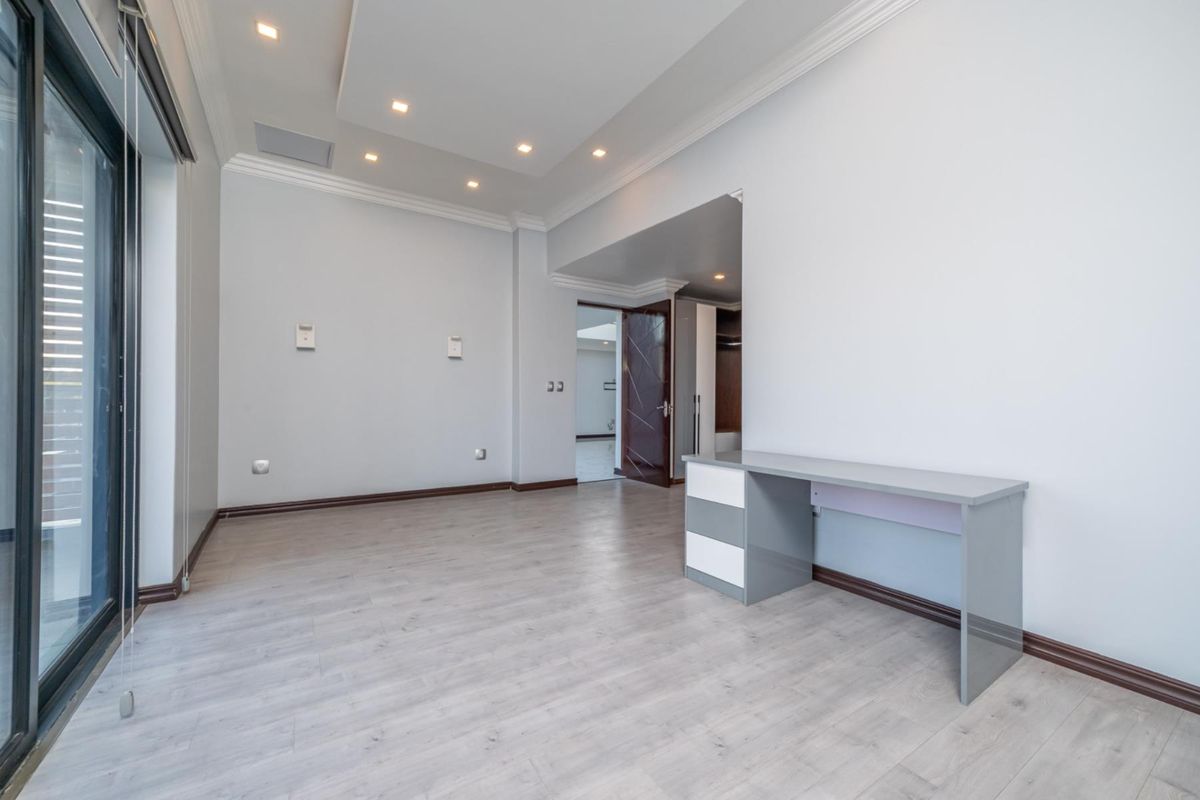 A bright, modern bedroom featuring recessed ceiling lighting, crown molding, laminate flooring, and a built-in desk, with access to an outdoor area via sliding doors.