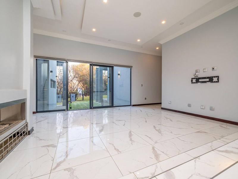 Spacious living room featuring high-gloss marble-look floor tiles, a built-in fireplace, and large sliding glass doors opening to the garden.