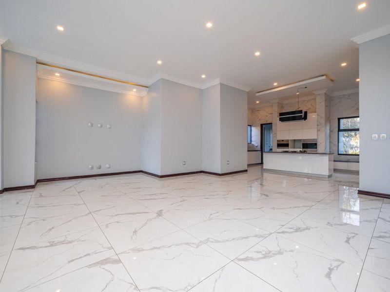 Spacious open-plan living and kitchen area featuring high-end marble-look floor tiles, modern recessed lighting, and a sleek, contemporary kitchen with integrated appliances.