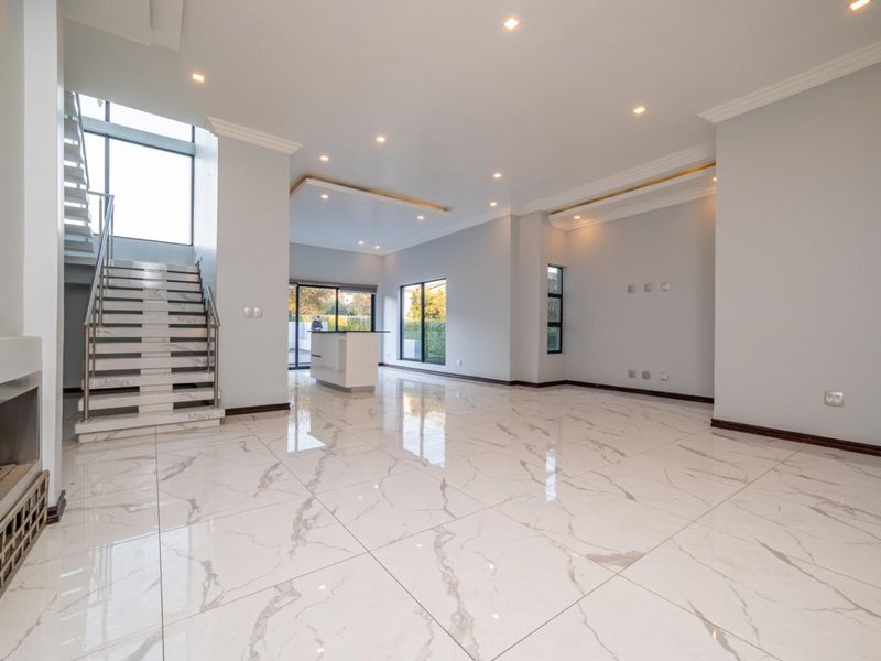Spacious open-plan living area featuring polished marble-look floor tiles, recessed lighting, a modern built-in fireplace, and a sleek staircase with metal balustrades.
