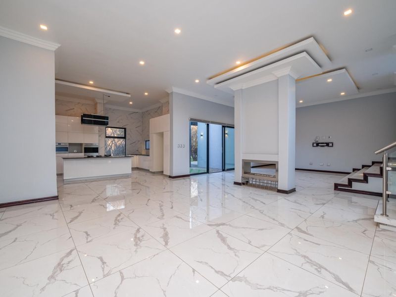 Spacious open-plan living area featuring high-end marble-look tiling, a central fireplace, modern kitchen with integrated appliances, and a sleek glass-railed staircase.