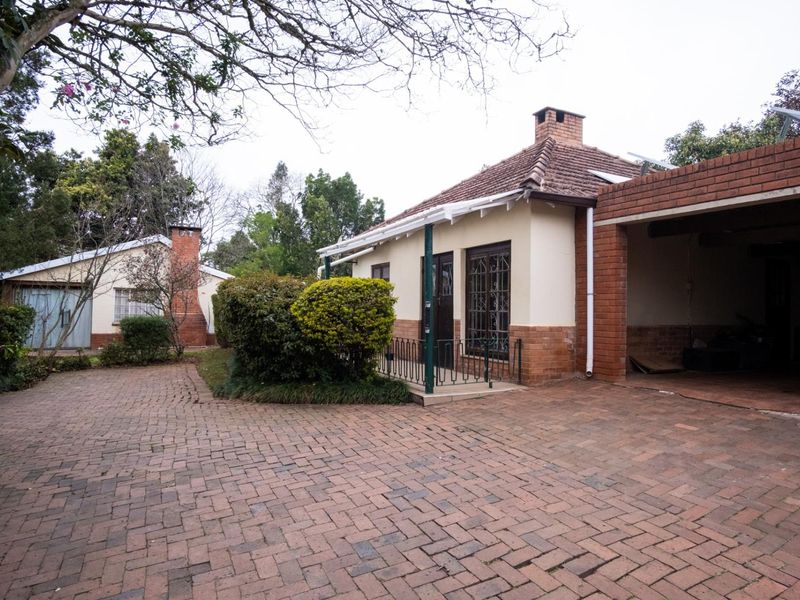 Front view of a single-story brick house featuring a paved driveway, attached carport, and established garden area.