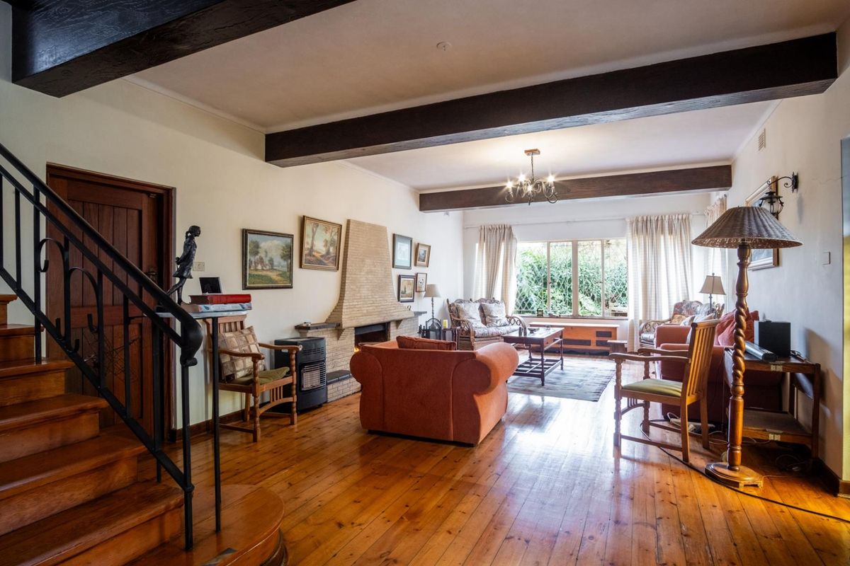 Spacious living room featuring exposed timber ceiling beams, a brick fireplace, and polished timber flooring with an adjoining staircase.