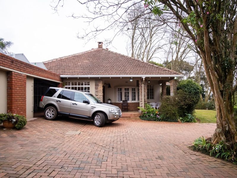 Front view of a charming house featuring a brick driveway, covered patio with stone pillars, and a tiled roof.