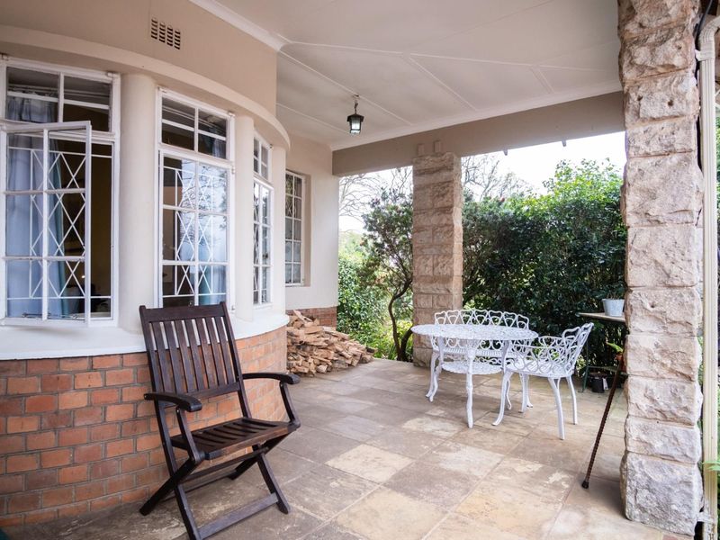 A covered patio area featuring stone pillars, brick detailing, and tiled flooring, providing a pleasant outdoor space overlooking the garden.