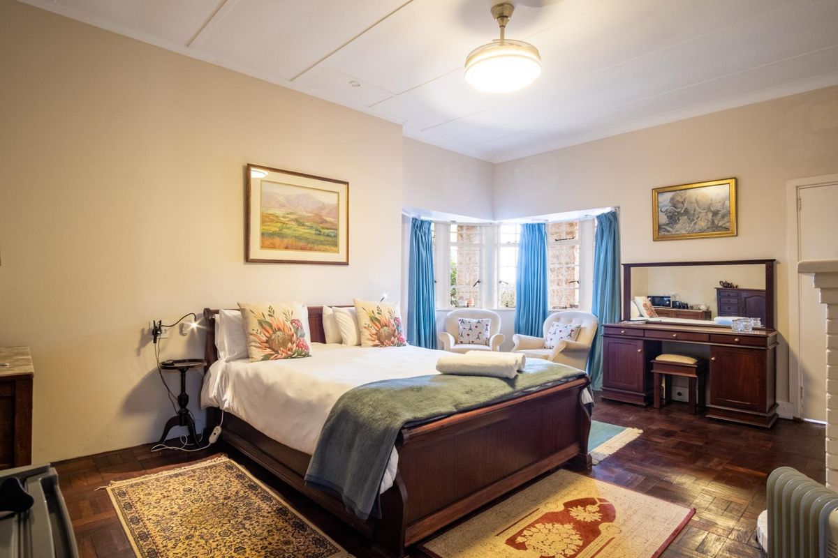 A spacious bedroom featuring classic parquet flooring, a charming bay window, and a traditional ceiling light fixture.