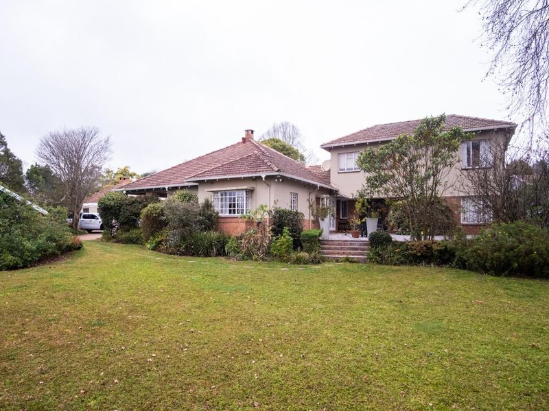 Rear view of a multi-level residential property featuring a tiled roof, brick and plaster facade, and a spacious garden with a paved terrace area.