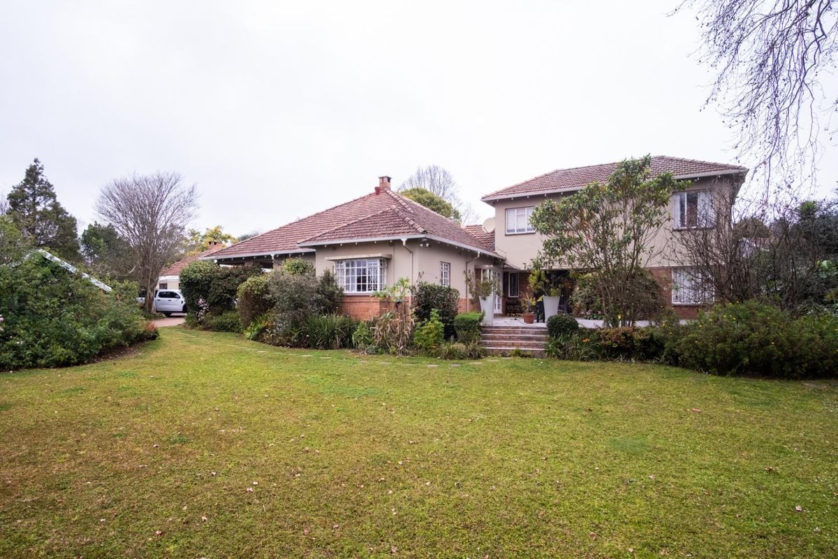 Rear view of a multi-level residential property featuring a tiled roof, brick and plaster facade, and a spacious garden with a paved terrace area.