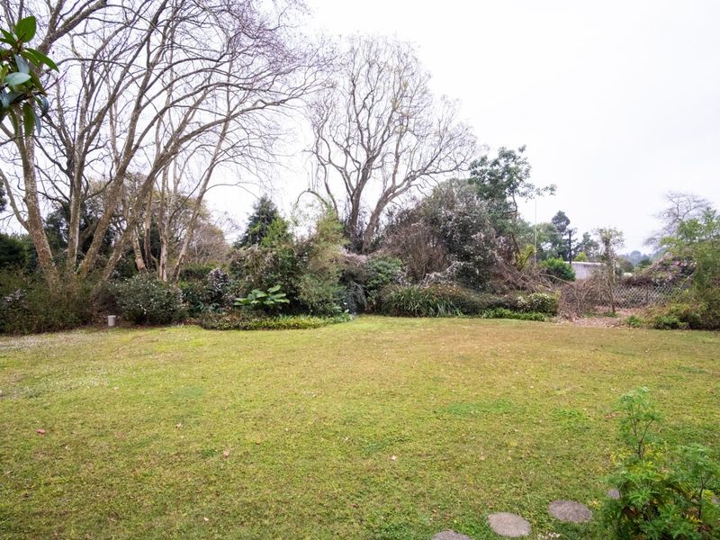 A spacious, established garden featuring a large lawn area, mature trees, and landscaped garden beds.