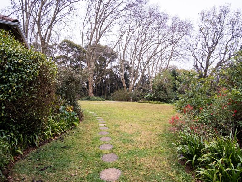 A spacious, well-established garden featuring a central lawn, mature trees, and a stone pathway leading through the landscaped grounds.
