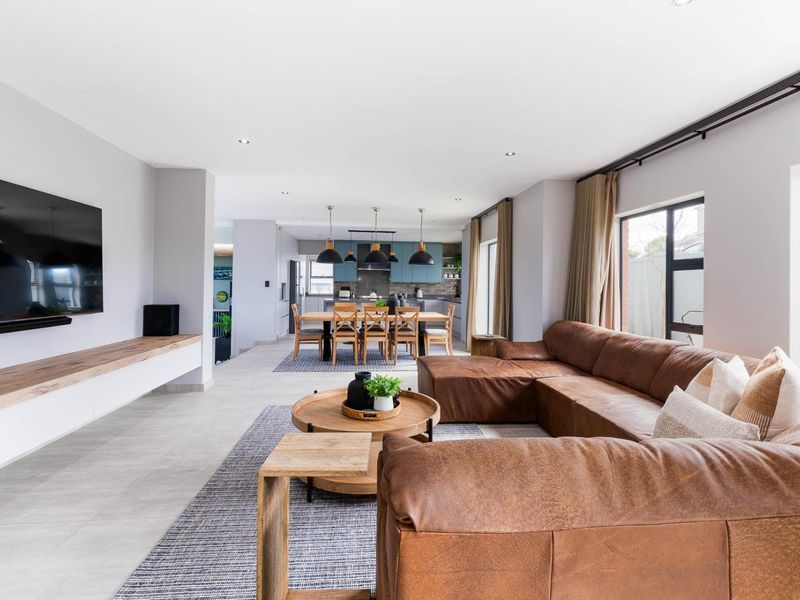 Spacious open-plan living and dining area featuring modern kitchen cabinetry, large format floor tiles, and integrated media storage.