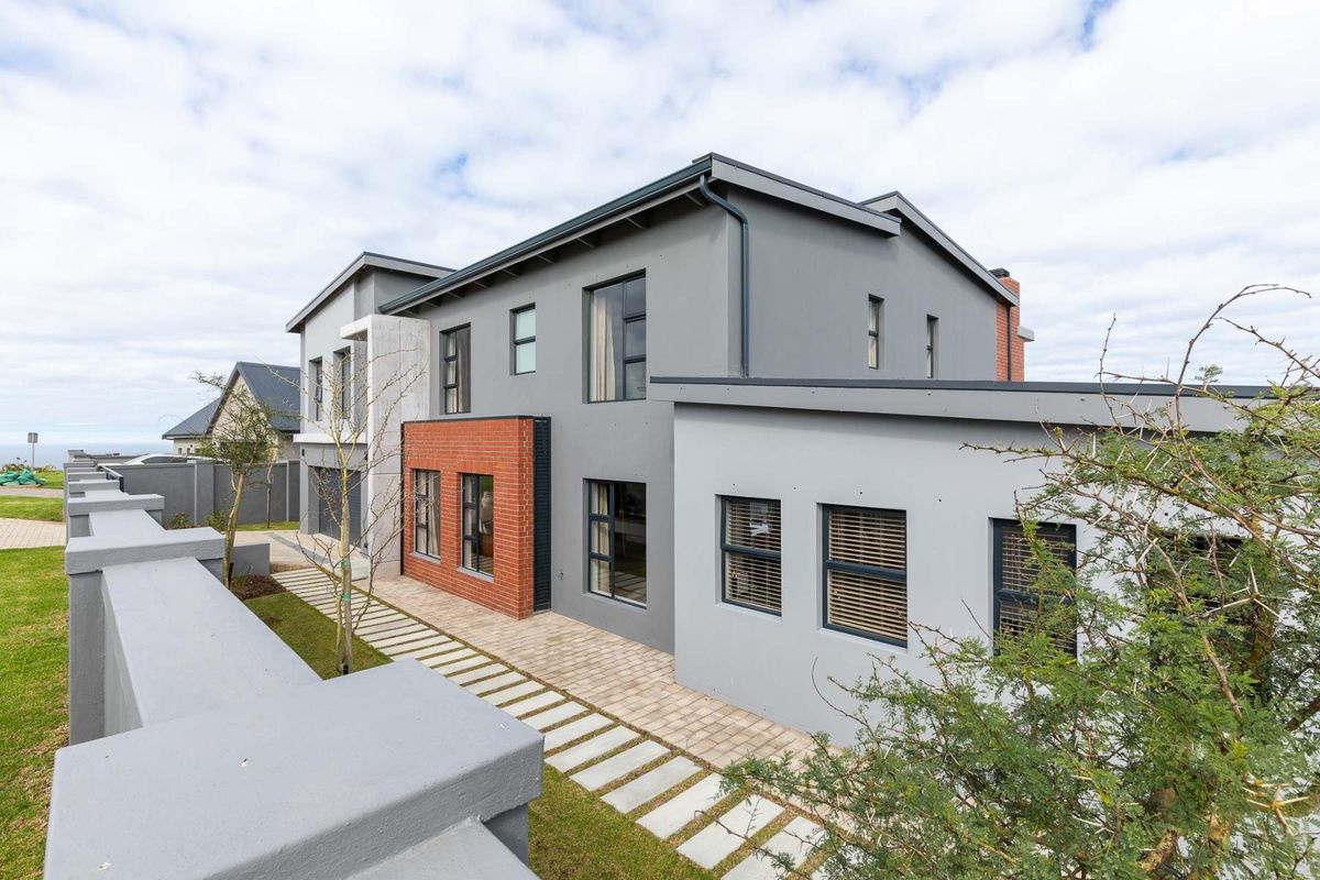 A modern double-storey residence featuring a combination of grey plastered walls and red brick accents, complemented by a paved walkway and boundary wall.