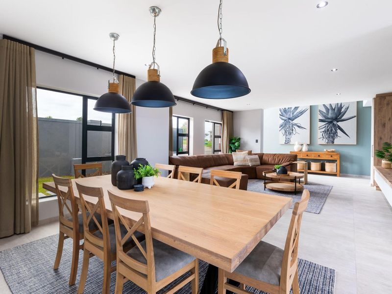 Spacious open-plan living and dining area featuring modern tiled flooring, contemporary pendant lighting, and large aluminium-framed windows providing ample natural light.