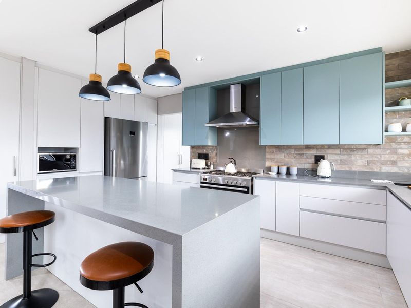 Modern kitchen featuring a large quartz island, sleek two-tone cabinetry, high-end built-in appliances, and stylish pendant lighting.