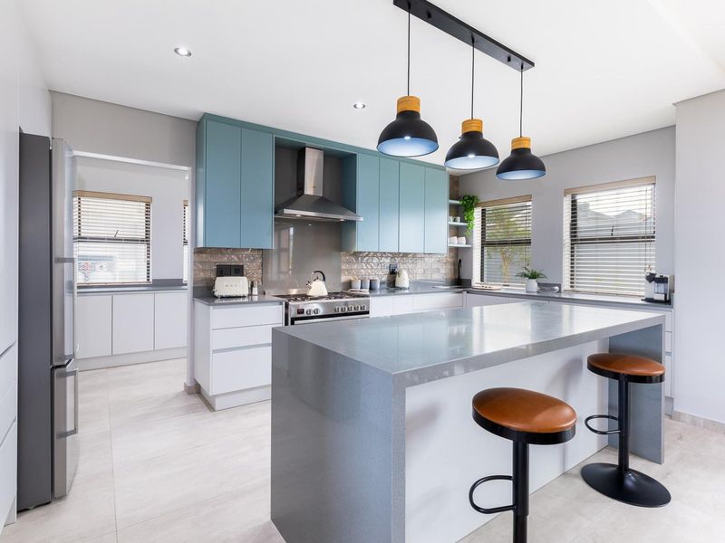 Modern kitchen featuring a large stone-topped island, blue and white cabinetry, stainless steel appliances, and stylish pendant lighting with tiled flooring.