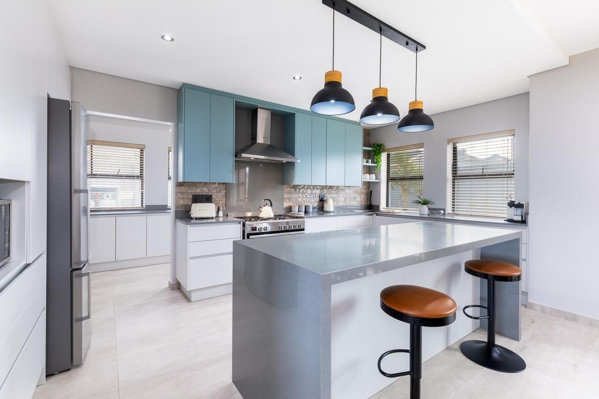 Modern kitchen featuring a large stone-topped island, blue and white cabinetry, stainless steel appliances, and stylish pendant lighting with tiled flooring.