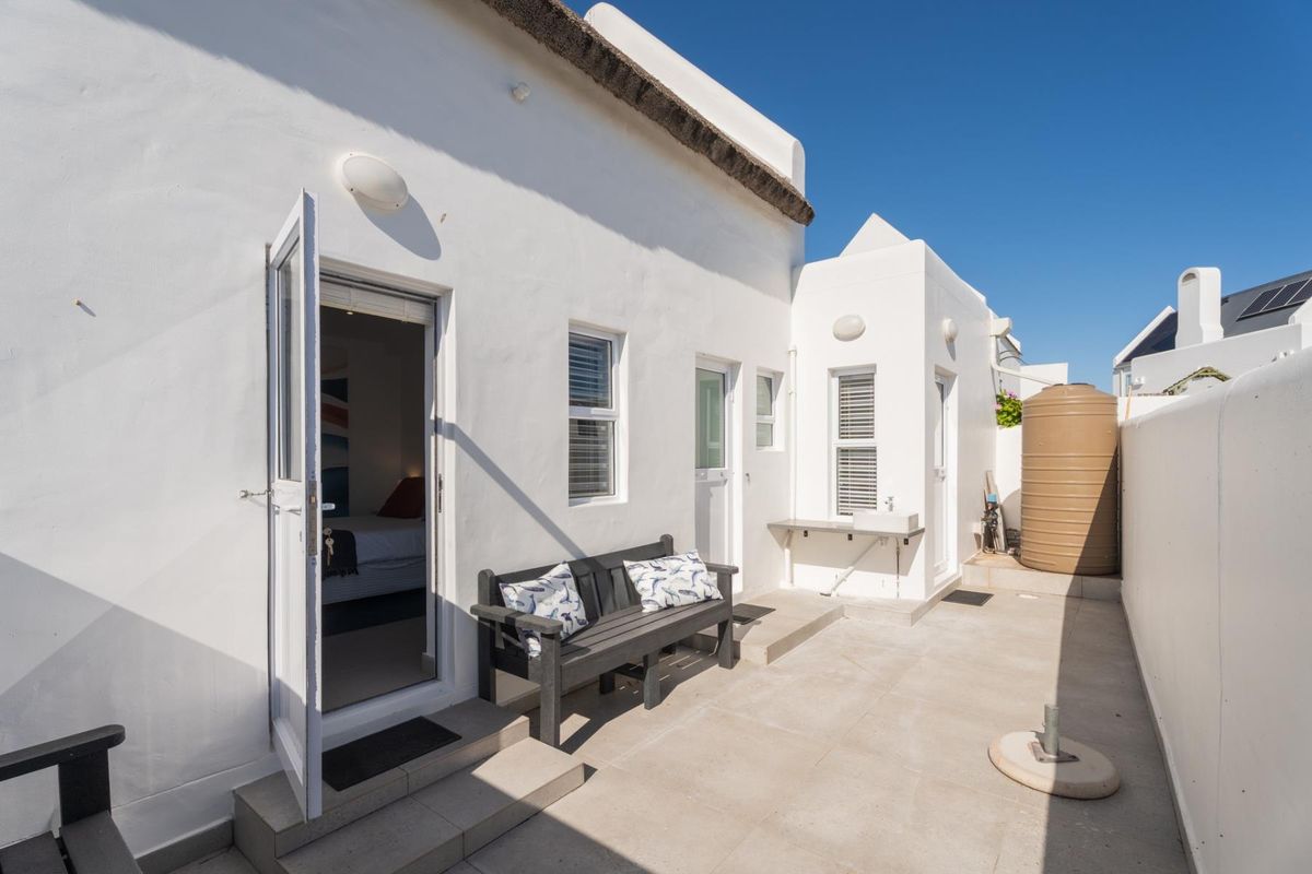 A clean rear exterior area featuring a thatched roof, tiled patio, external wash basin, and a water storage tank.