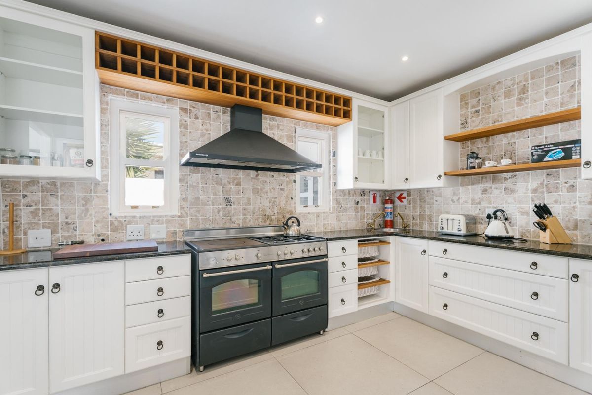 A well-appointed kitchen featuring white cabinetry, granite countertops, a dual oven with gas hob, and a decorative tiled backsplash.