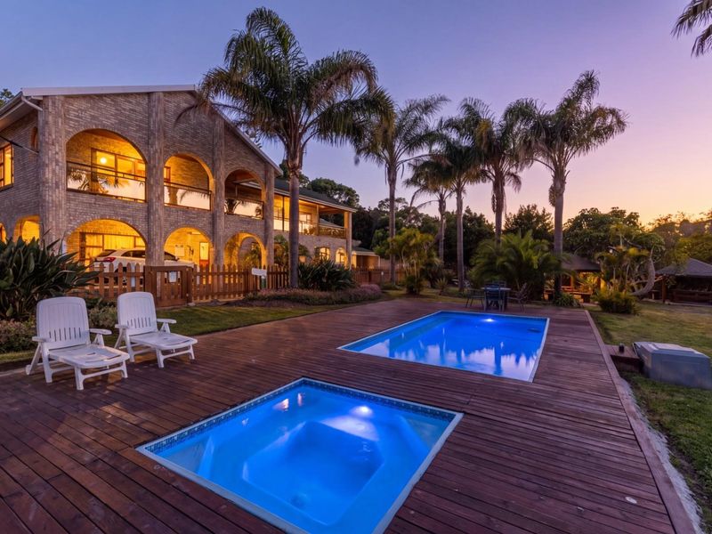 A beautifully lit outdoor pool area featuring a swimming pool, integrated spa, and timber decking, set against a charming brick guest house facade.