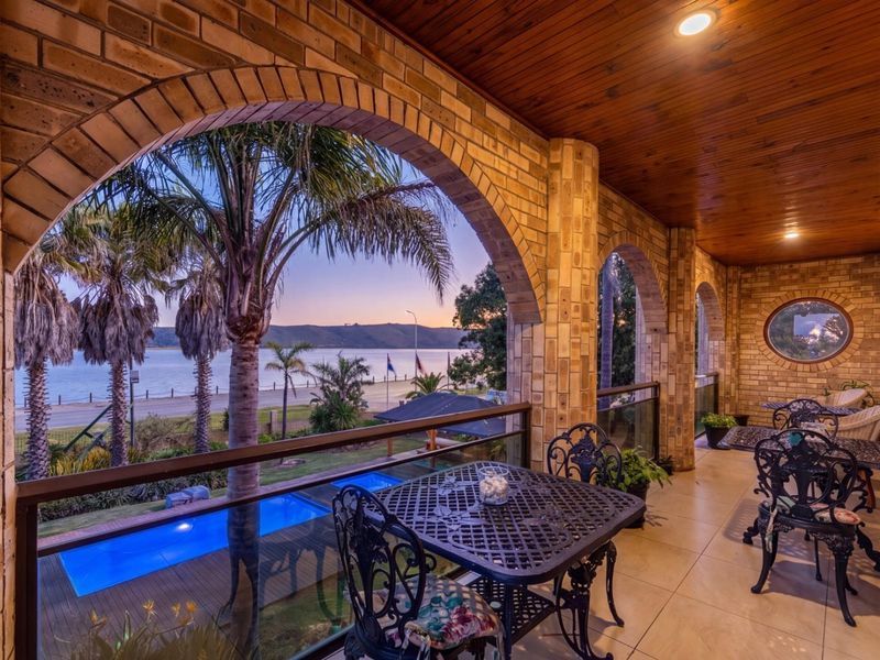 Spacious covered balcony featuring brick arches, timber ceiling, and glass balustrades, offering scenic views over the pool and waterfront.