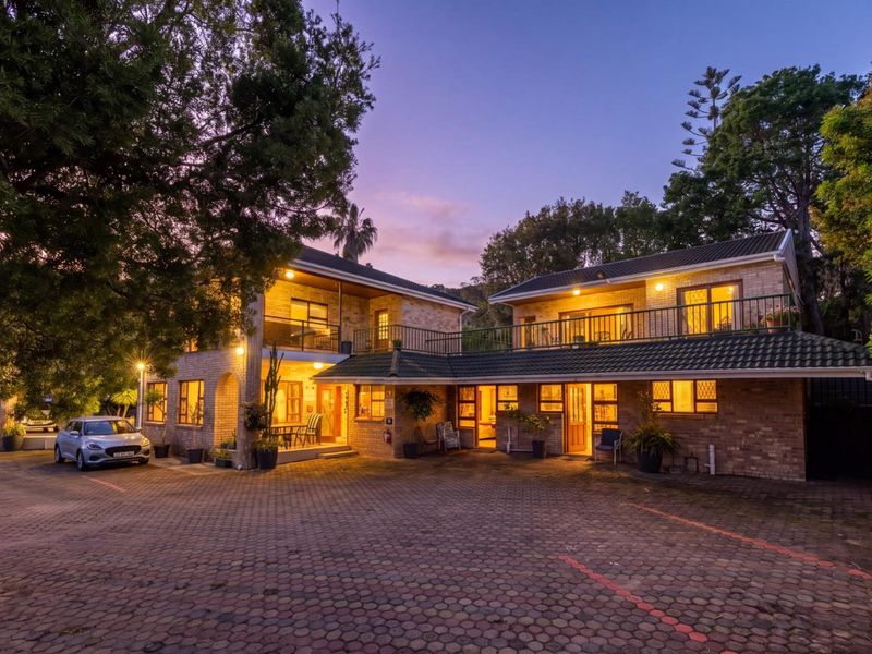 A well-maintained double-story guest house featuring a brick facade, paved driveway, and upper-level balconies, captured during twilight.