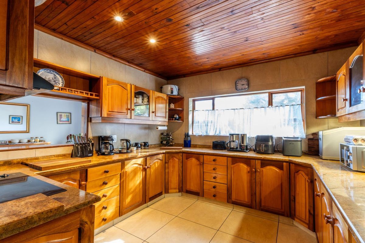A traditional kitchen featuring extensive wooden cabinetry, laminate countertops, and a warm timber-paneled ceiling with recessed lighting.