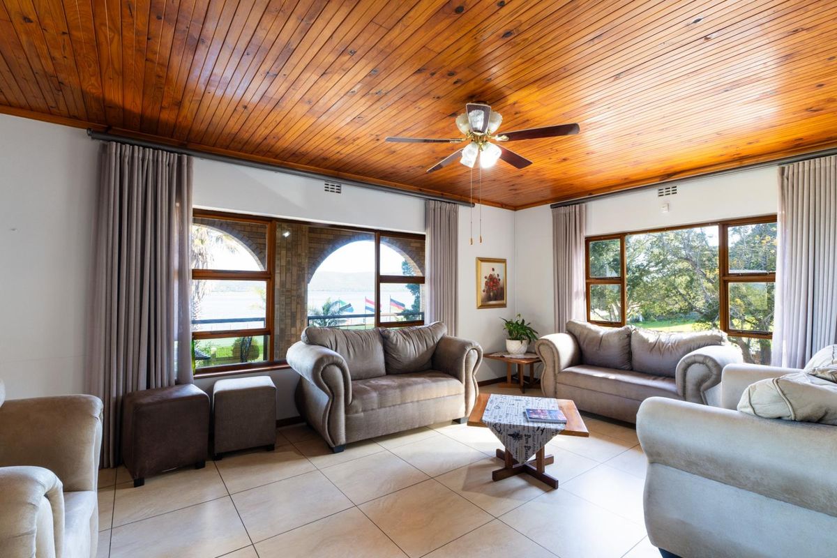 Spacious living room featuring a warm timber tongue and groove ceiling, tiled flooring, and large windows providing ample natural light and garden views.