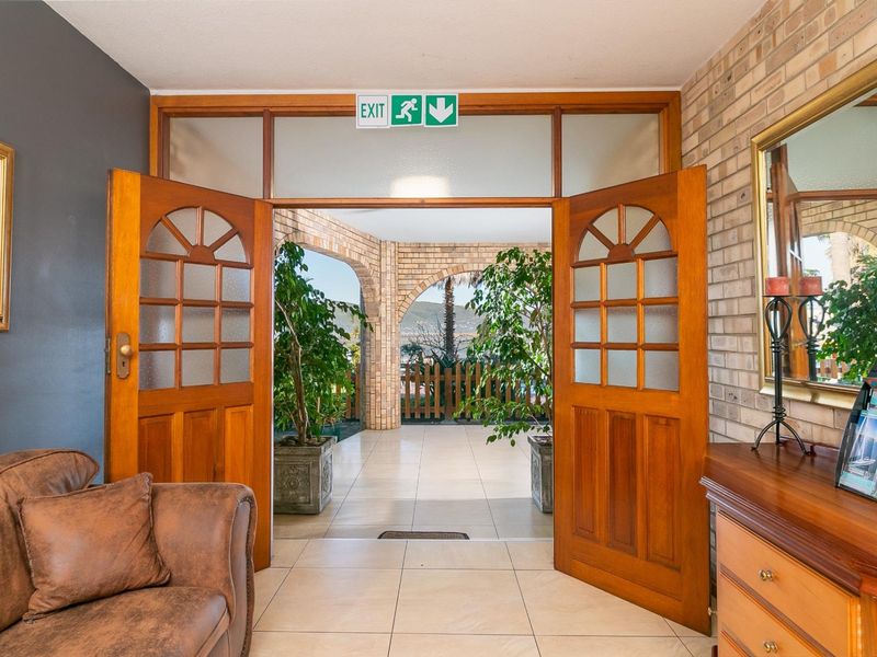 Welcoming entrance area featuring double timber doors, brick accent wall, and tiled flooring, providing direct access to the outdoor patio area.