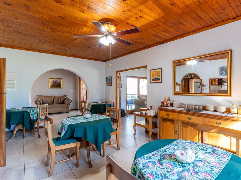A spacious dining area featuring a warm timber ceiling, tiled flooring, and a distinctive architectural archway leading to an adjacent living space.