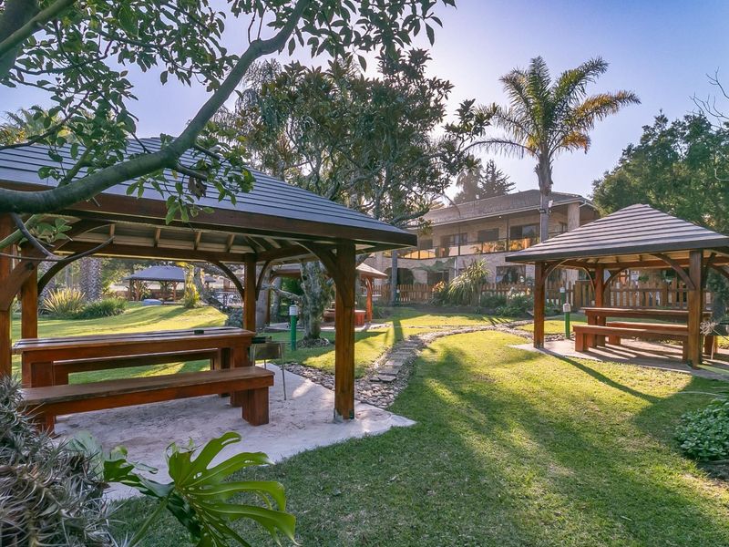 A well-maintained garden area featuring multiple timber gazebos, paved pathways, and lush landscaping, providing an inviting outdoor space for guests.