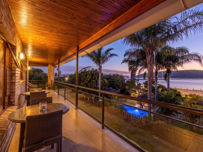 Spacious covered balcony featuring a timber ceiling, glass balustrade, and tiled flooring, offering scenic views of the garden, pool, and waterfront.