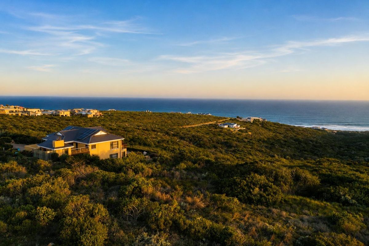 An aerial view of a residential property situated in a coastal landscape with ocean views and solar panels installed on the roof.