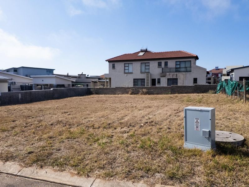 A vacant residential plot featuring a level grass surface, boundary wall, and utility connection points, situated in a developed neighborhood.