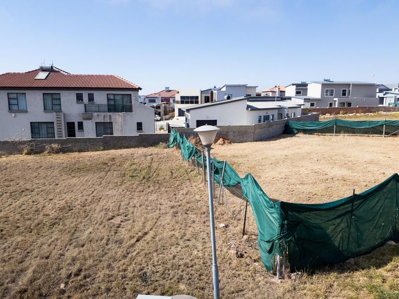 A vacant residential plot featuring a boundary wall and temporary fencing, situated in a developed neighborhood.