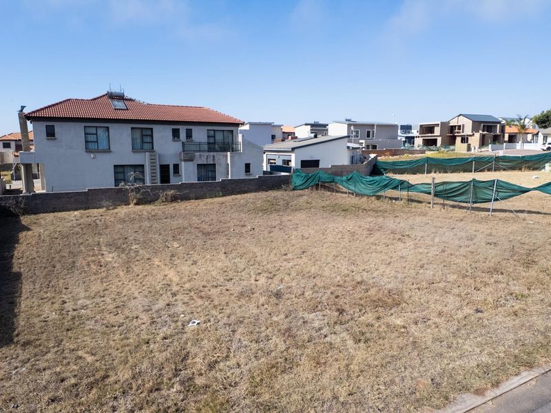 A vacant residential plot of land featuring perimeter boundary walls and temporary fencing, situated in a developed suburban neighborhood.