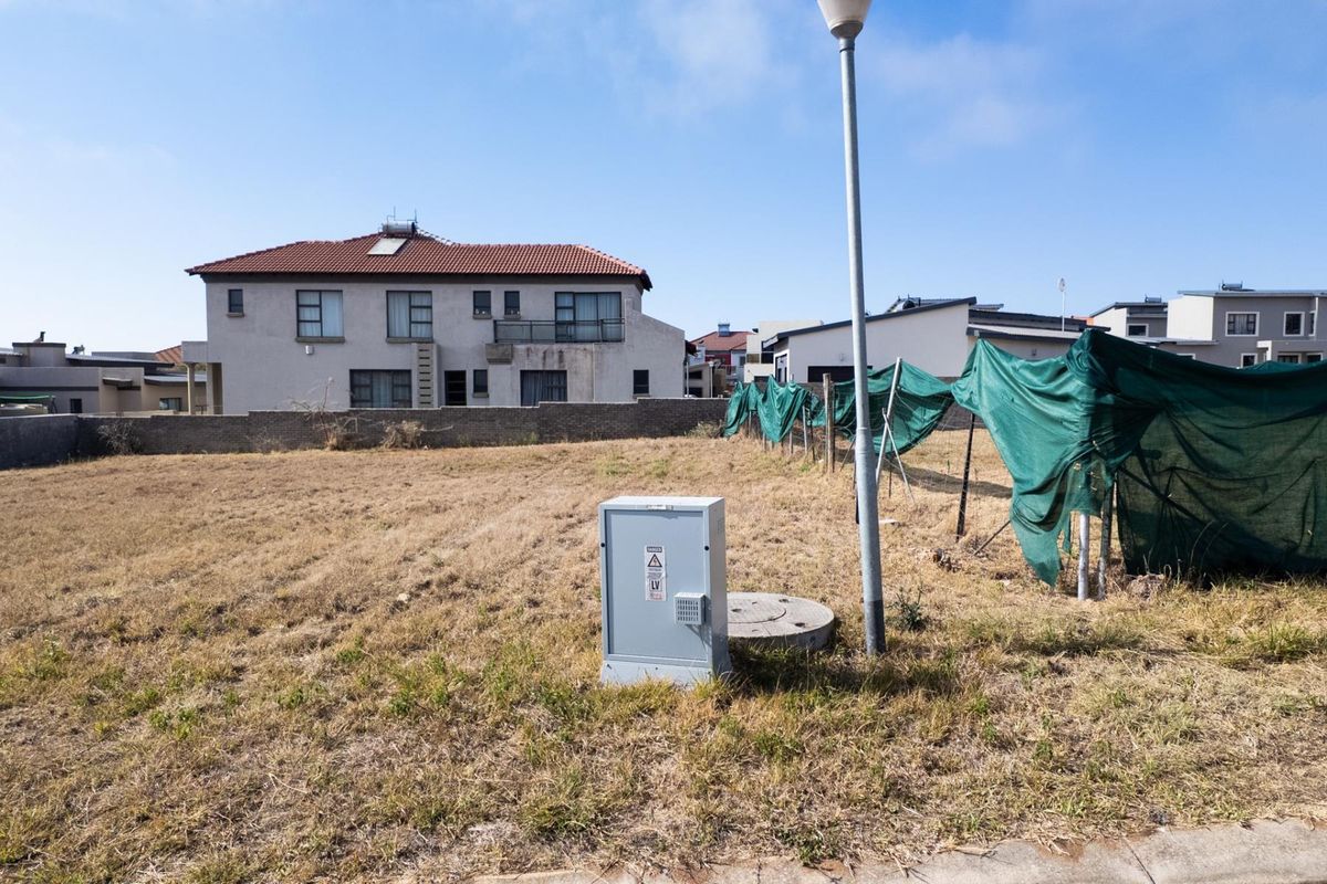 A vacant residential plot featuring an electrical distribution box, street light, and boundary wall, situated in a developed neighborhood.