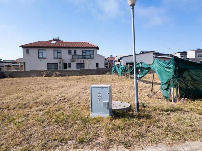 A vacant residential plot featuring an electrical distribution box, street light, and boundary wall, situated in a developed neighborhood.