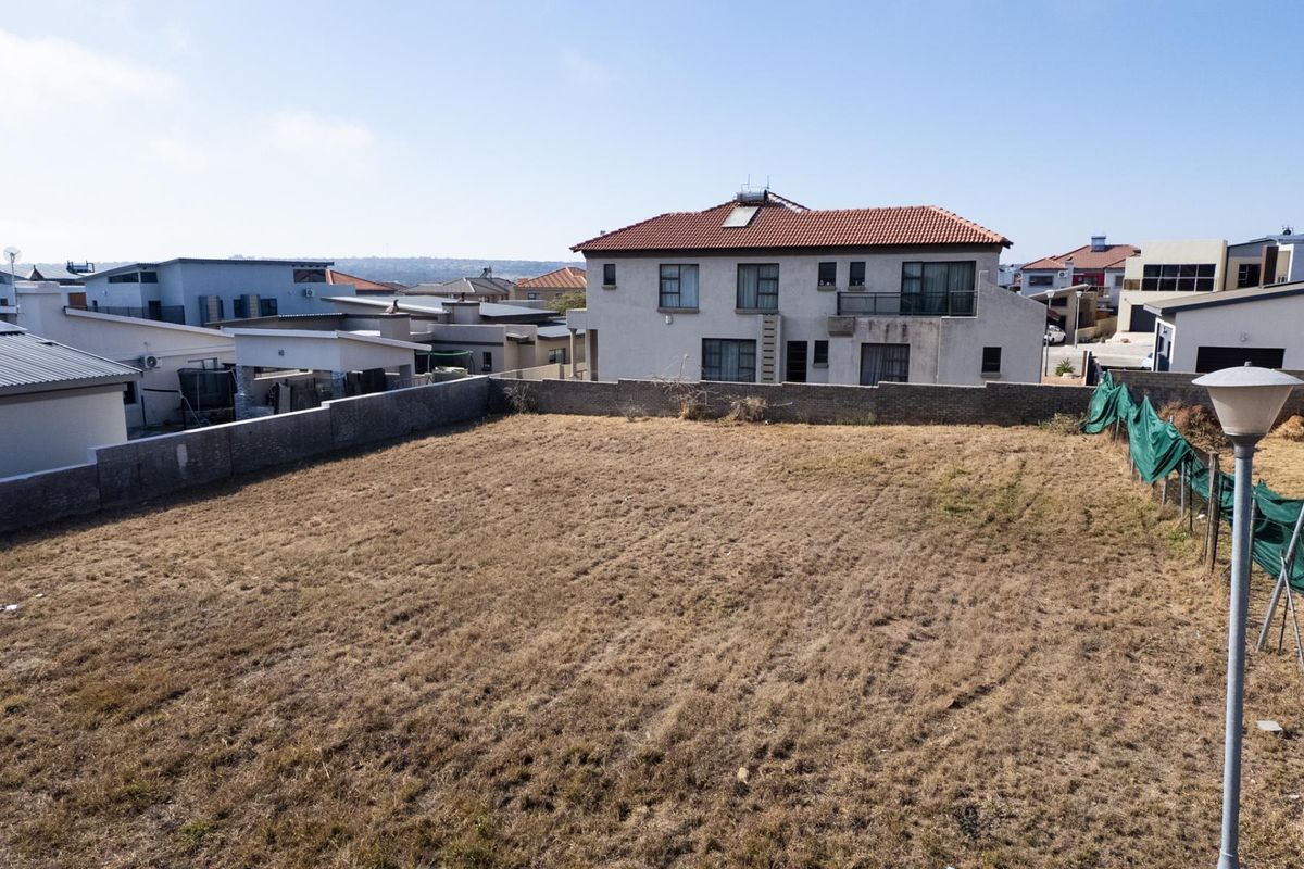 A vacant residential plot of land enclosed by a perimeter brick wall, situated in a developed suburban neighborhood.
