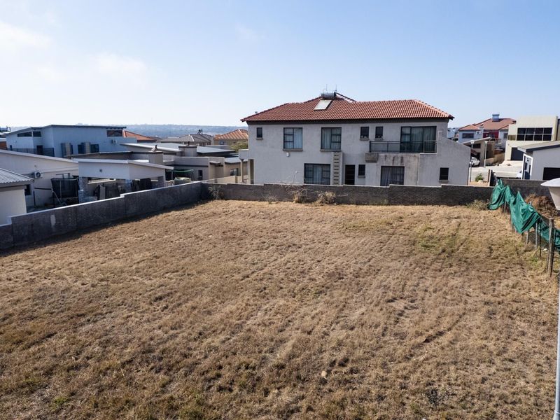A vacant residential plot of land enclosed by a perimeter brick wall, situated in a developed suburban neighborhood.