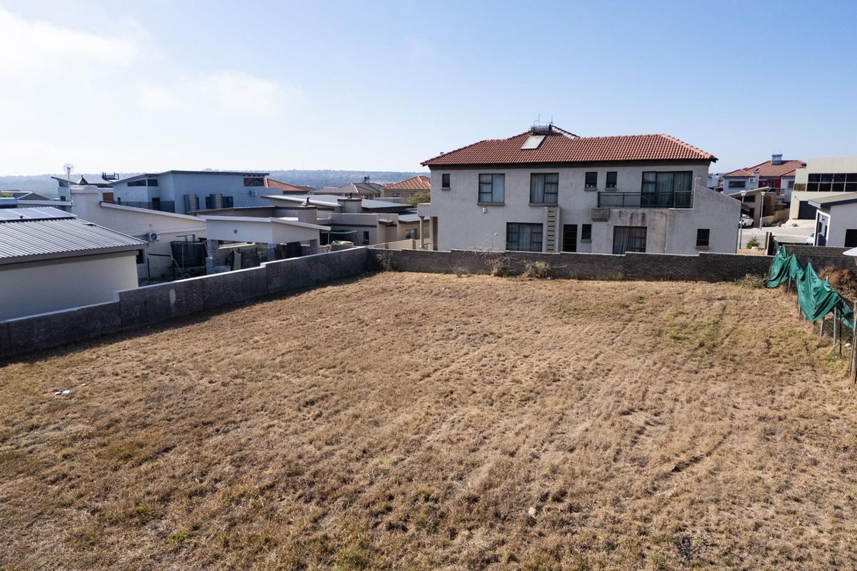 A vacant residential plot of land enclosed by boundary walls, situated within a developed suburban neighborhood.